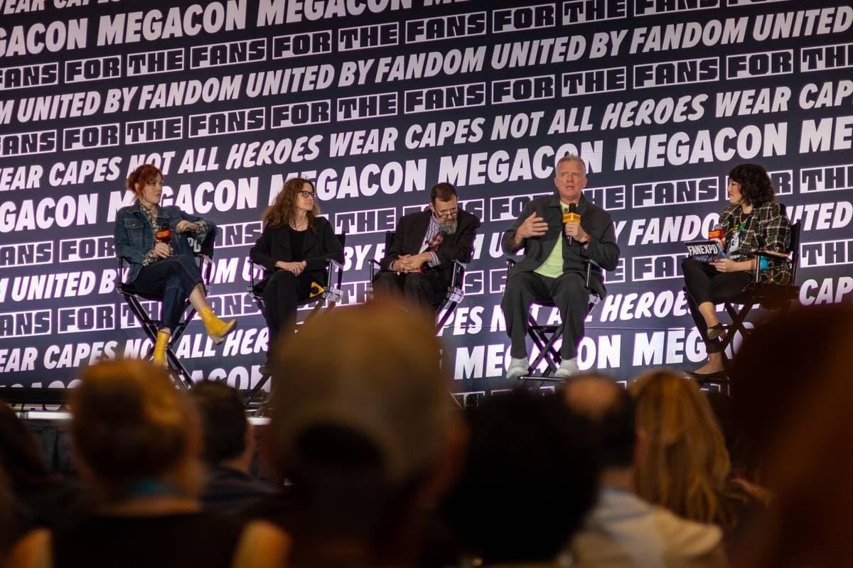 Four cast members seated on stage in front of a purple MegaCon backdrop, an audience in the foreground