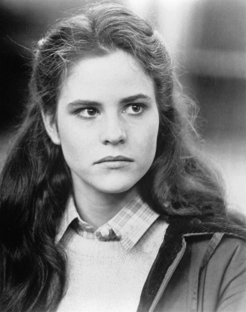 Ally Sheedy at 19, long hair, plaid collar and sweater, looking sideways, black and white