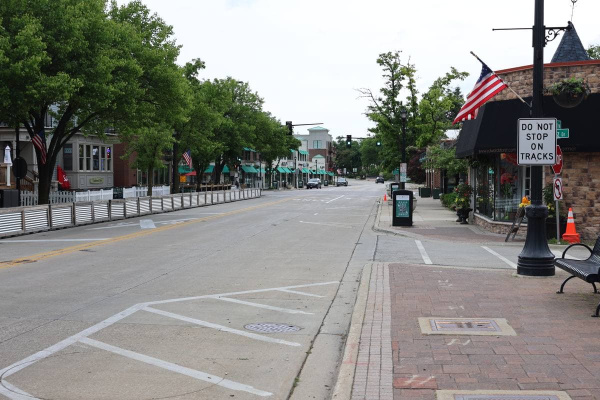 A wide quiet street with brick shopfronts, trees and a railway crossing sign