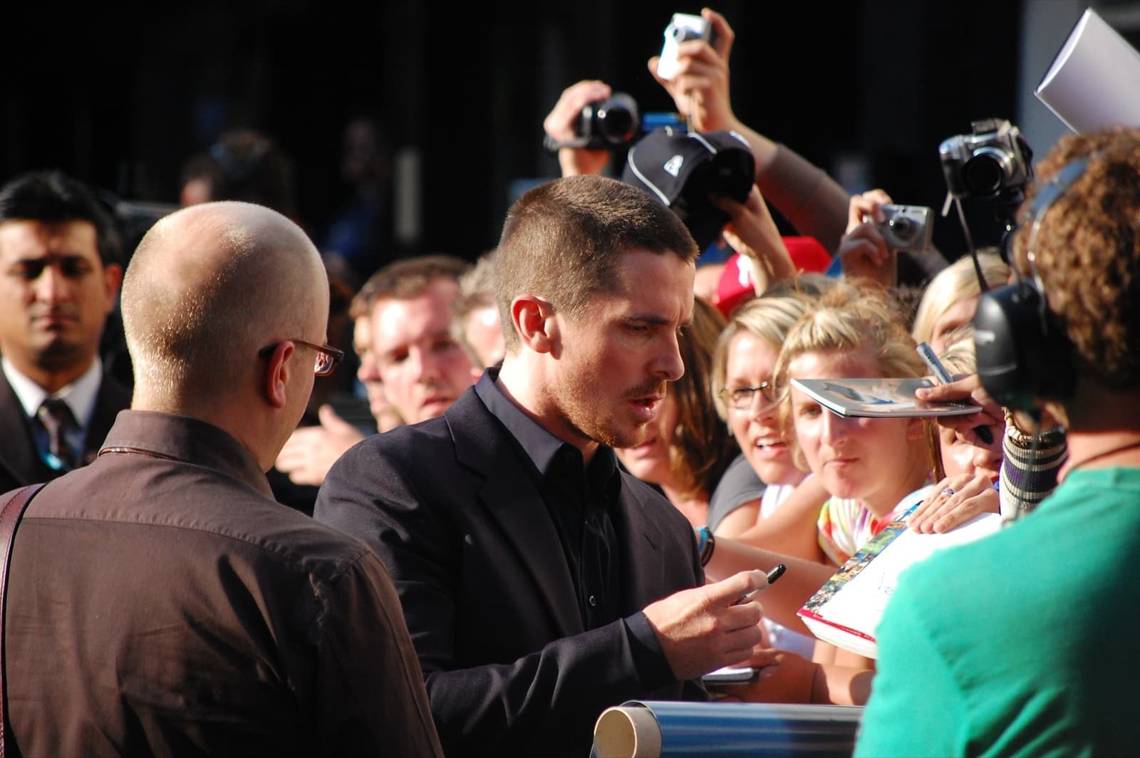 Christian Bale signing autographs for a crowd of fans with cameras