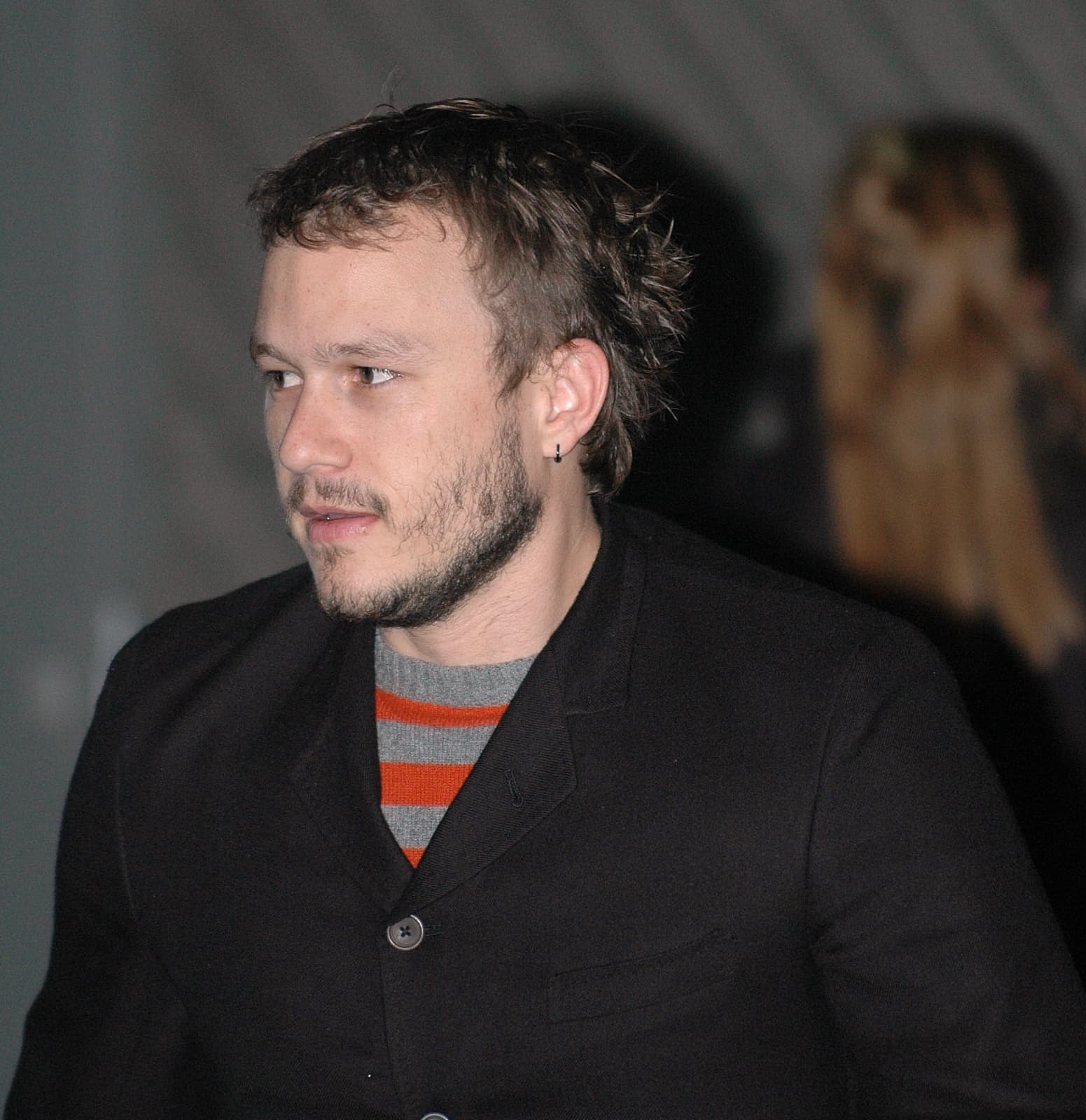 Heath Ledger in a dark jacket and striped jumper, looking to one side