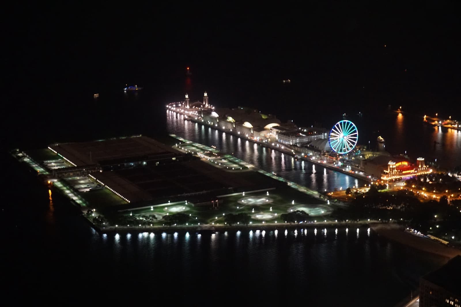 A long pier lit up on black water, with a big wheel at its middle
