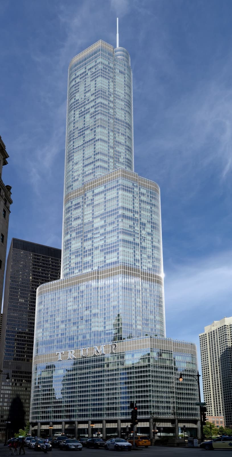 A stepped glass skyscraper with a spire beside the Chicago River