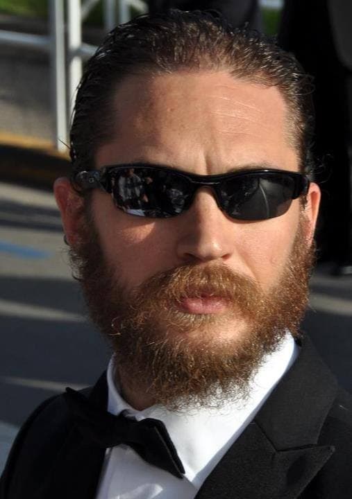 Tom Hardy with a full beard and slicked hair in dark glasses and a bow tie