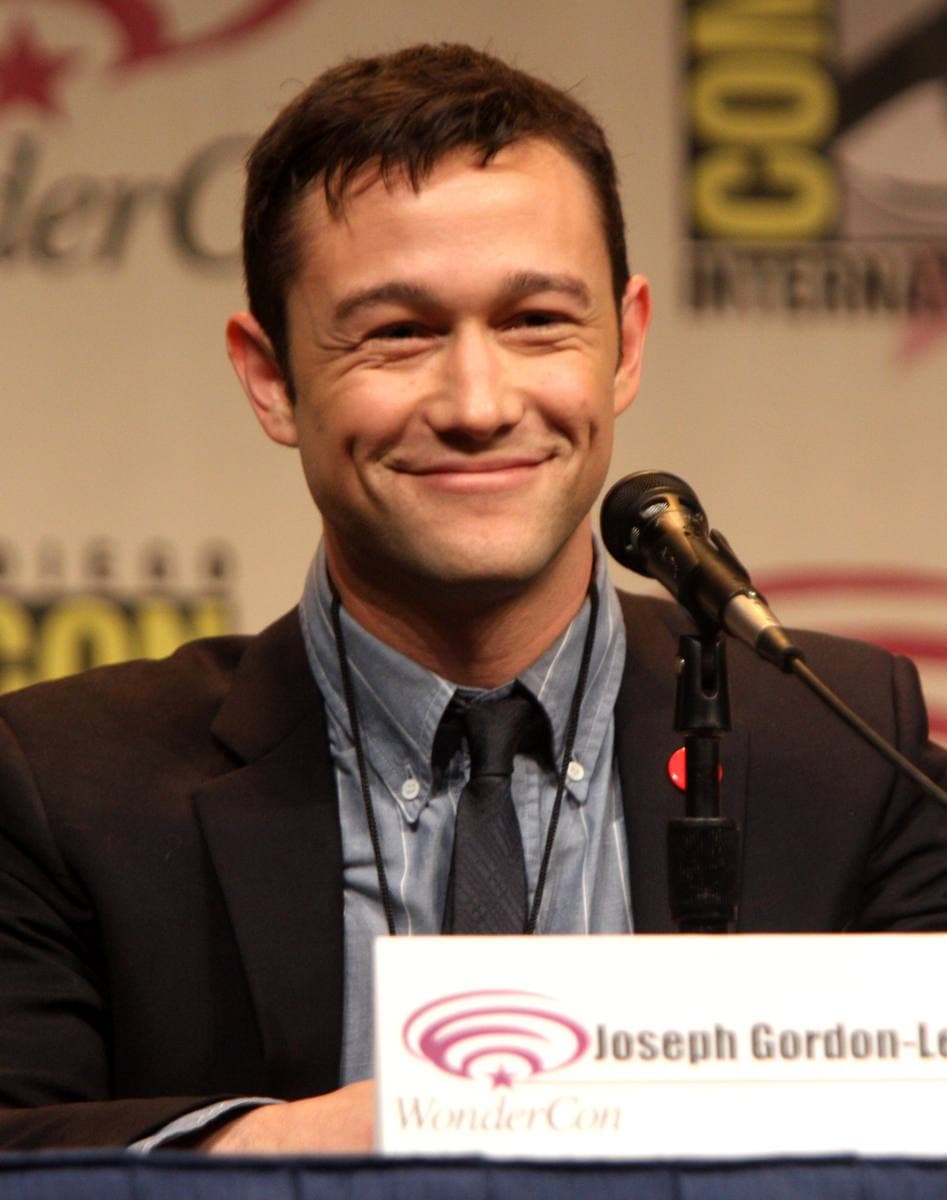 Joseph Gordon-Levitt smiling at a panel microphone in a suit and tie