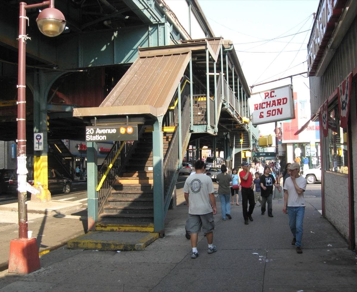 Street-level view under an elevated train line with a station stair and shops