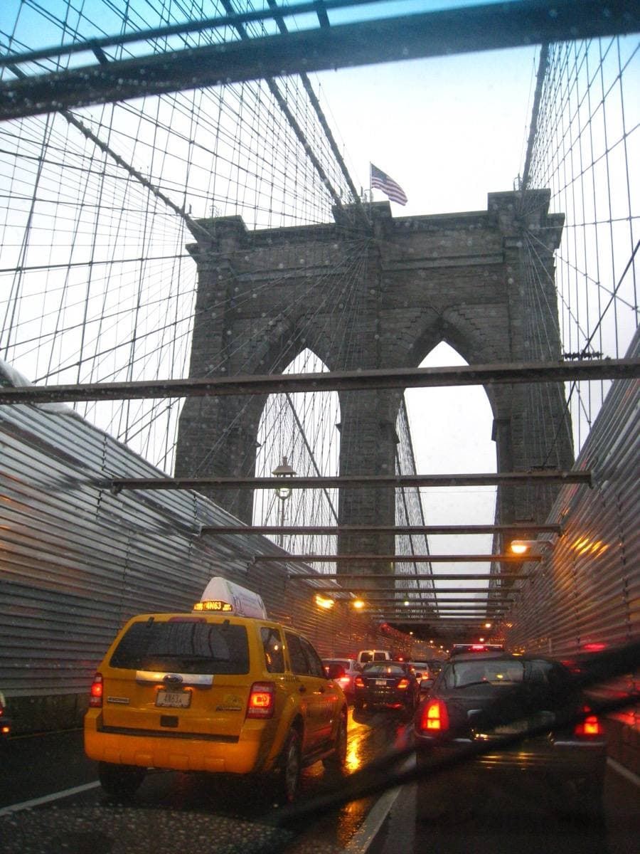 A yellow taxi on the Brooklyn Bridge roadway under the stone tower and cables