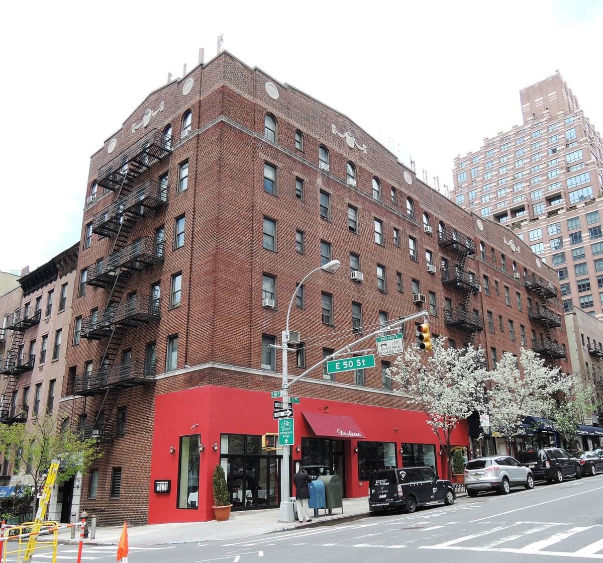 A red-brick corner building with a red awning on First Avenue