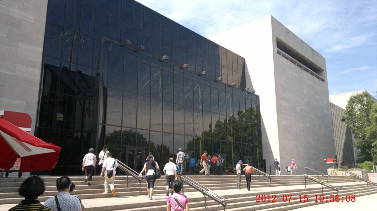 Glass-and-stone museum building with steps and visitors