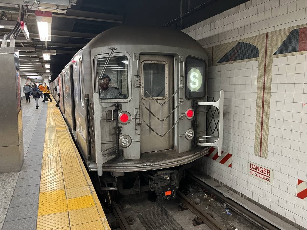 A silver S shuttle train at a tiled platform