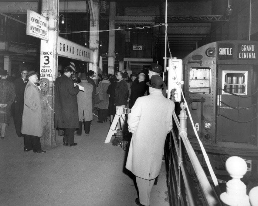 Black-and-white photograph of commuters on the Grand Central shuttle platform beside a train