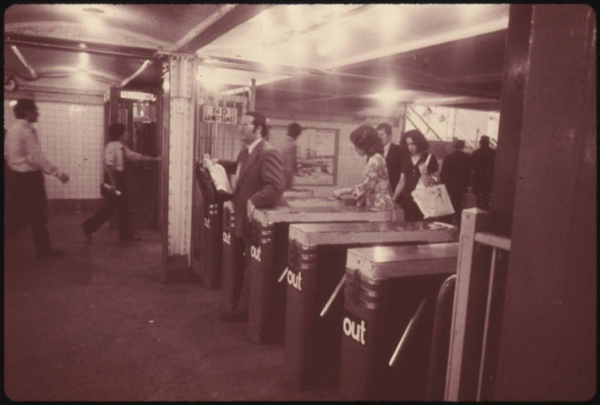 Colour photograph from 1974 of passengers pushing through subway turnstiles