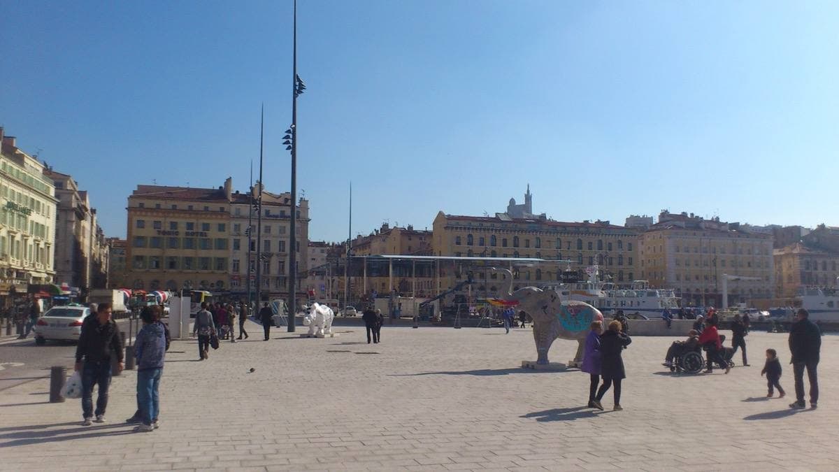 A wide sunny quay with people walking and a hill church in the distance
