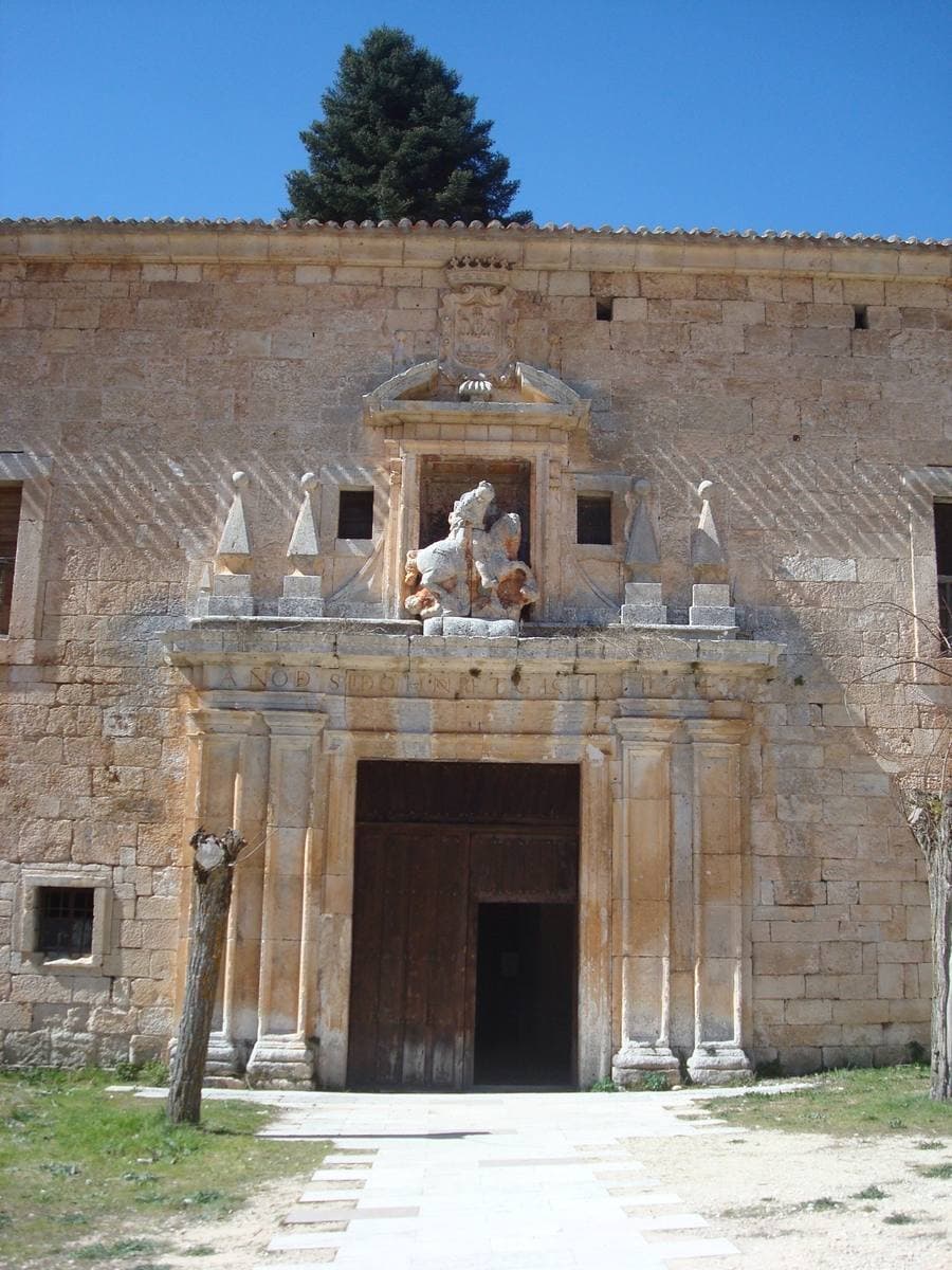 A stone monastery gateway with a sculpted horseman above the door and a fir tree behind