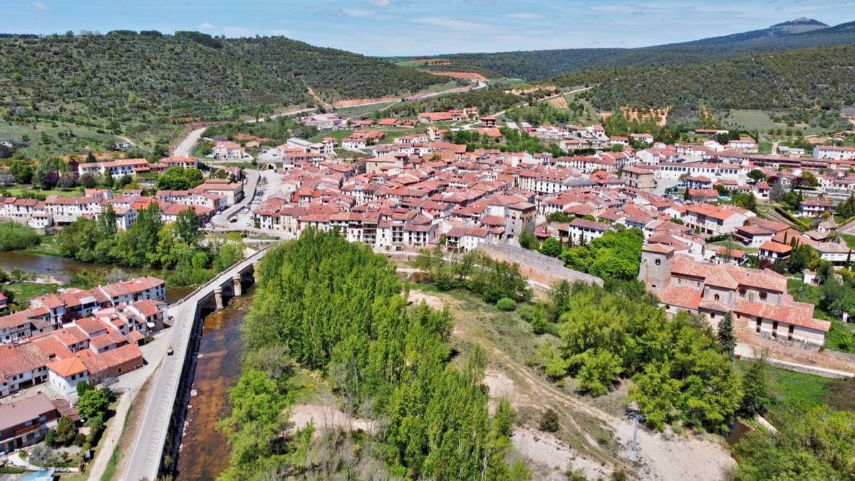 Red roofs of a village beside a river and a bridge, green hills behind