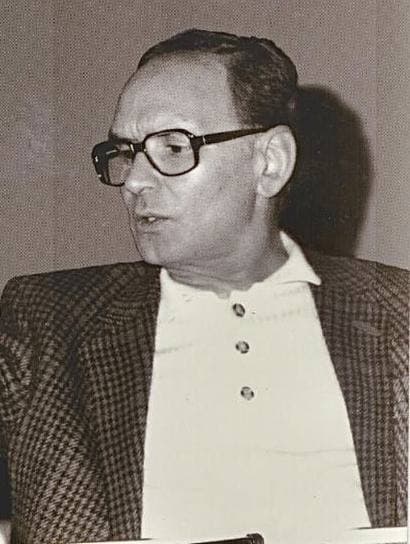 Ennio Morricone in glasses and a checked jacket, seated, turning to speak