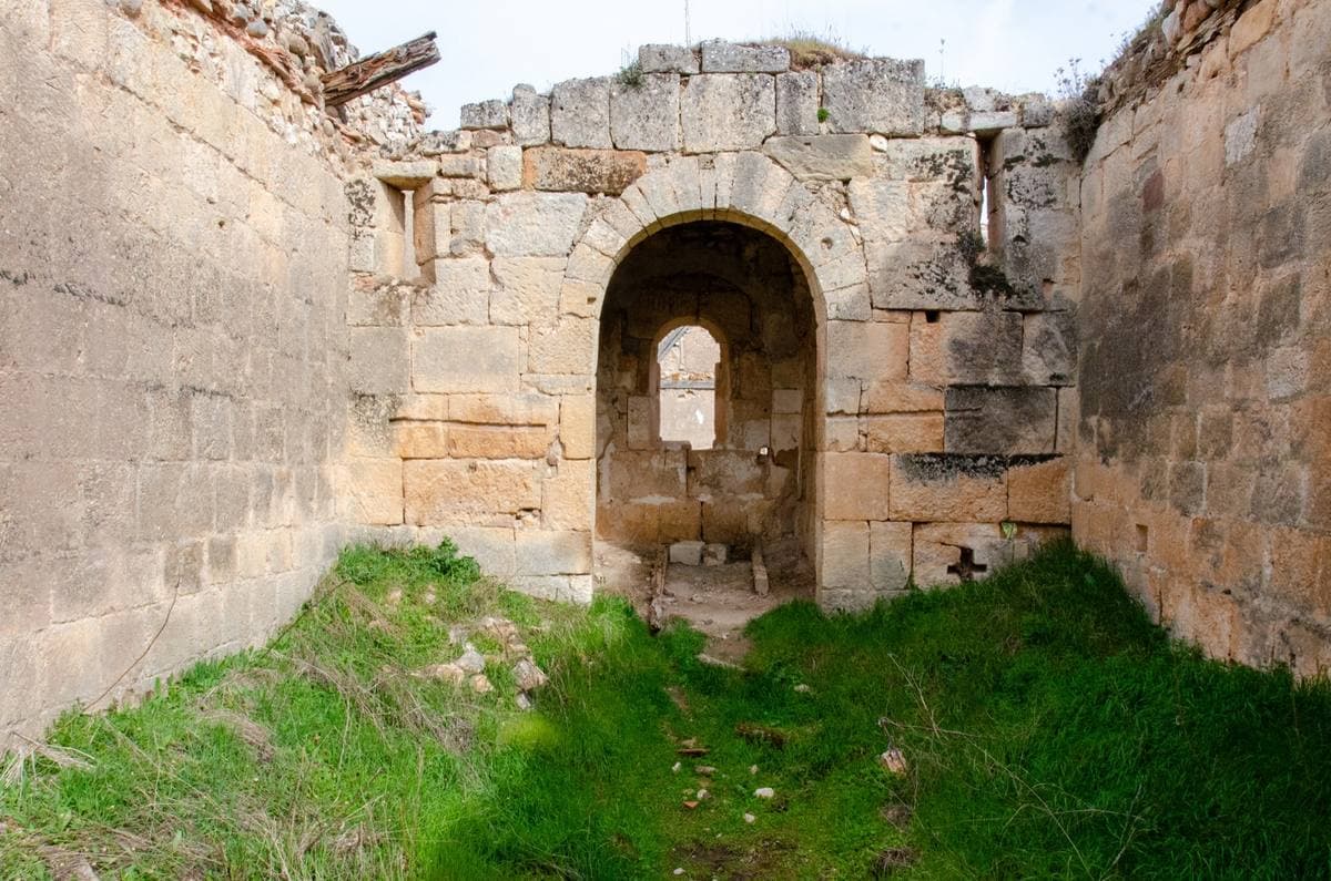 A ruined stone chapel with an arched niche, grass growing inside