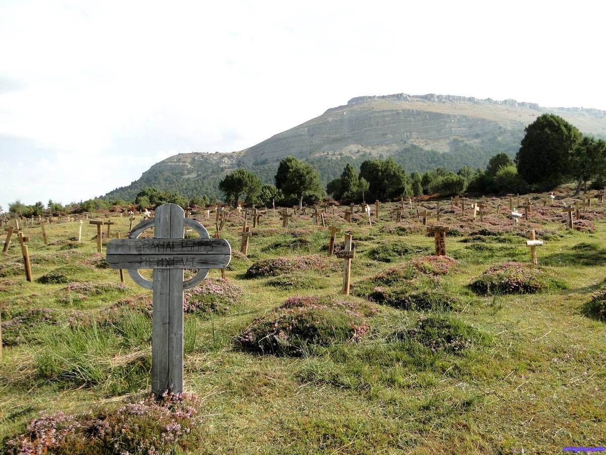 A weathered wooden cross among rows of graves under a flat-topped ridge