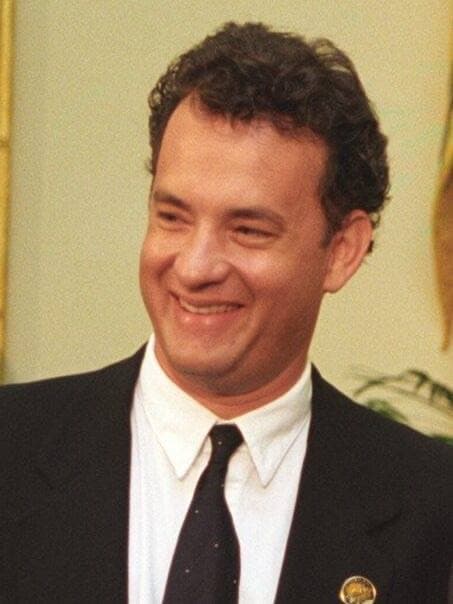 Tom Hanks in a dark suit, smiling, 1995