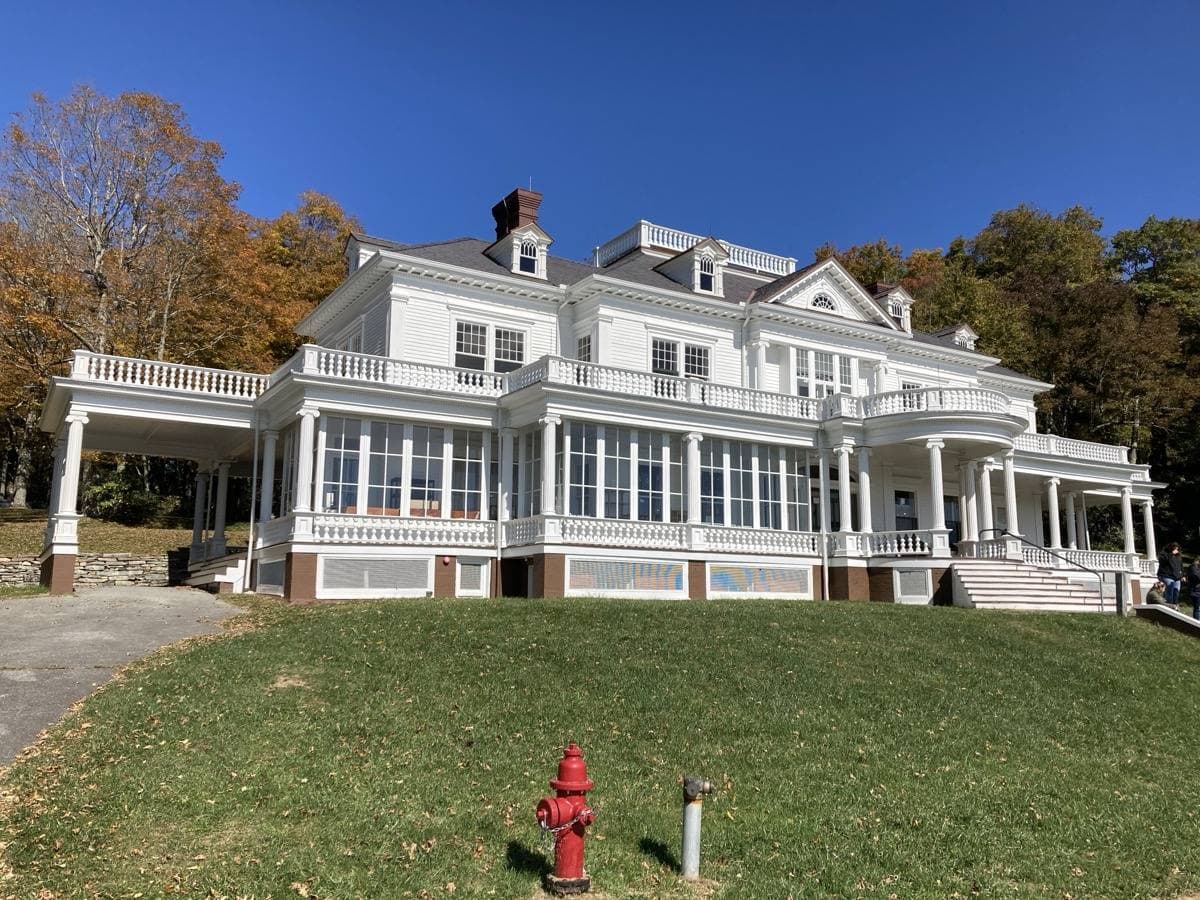 The white Colonial Revival front of Flat Top Manor with its long porch, 2022