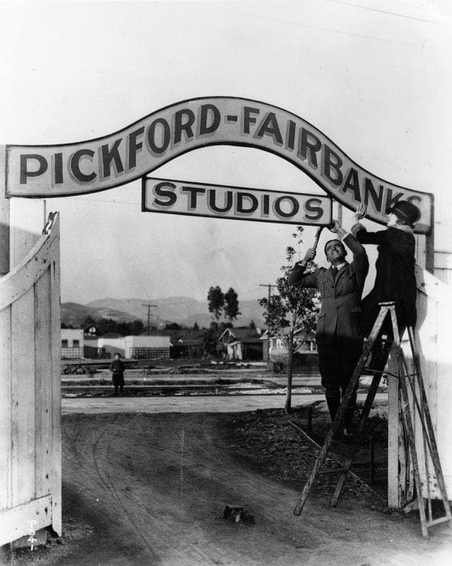 Mary Pickford and Douglas Fairbanks on a ladder hanging a studio sign, 1922