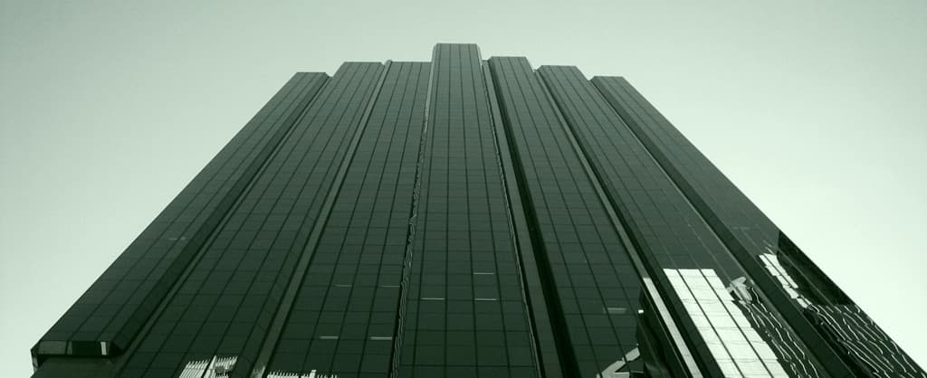 A dark glass office tower seen from below, tinted green