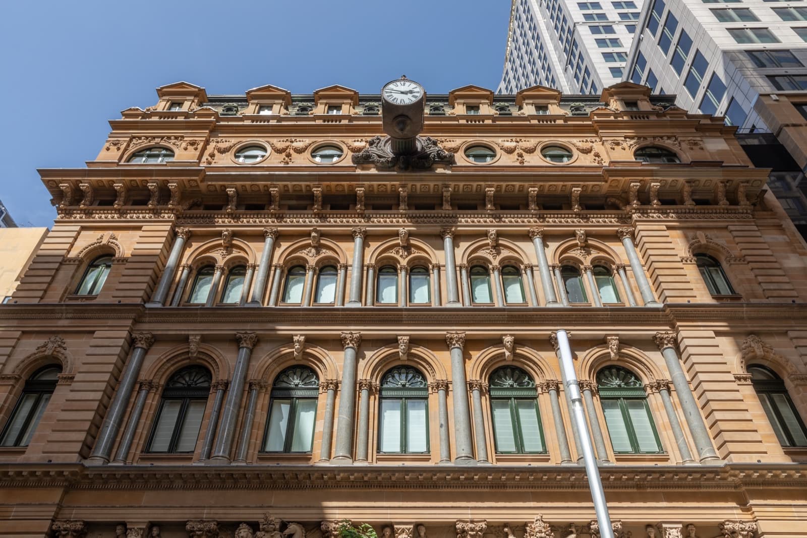A long sandstone building with arcades and a clock tower on a city street