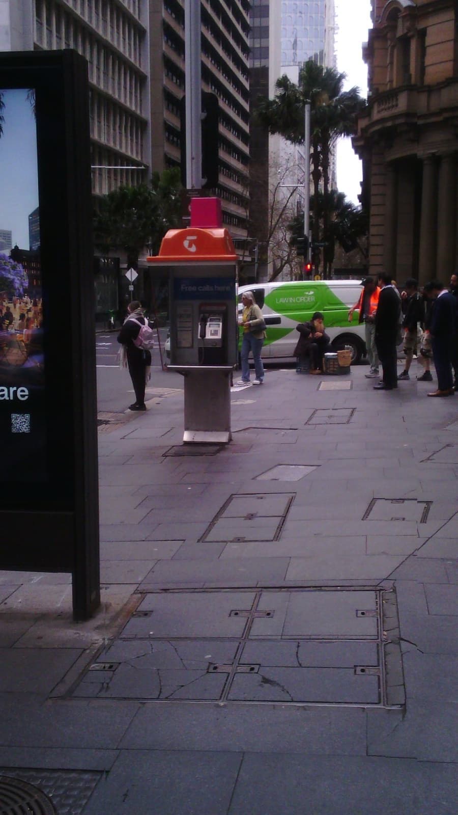 The payphone on the corner with people and a van behind it
