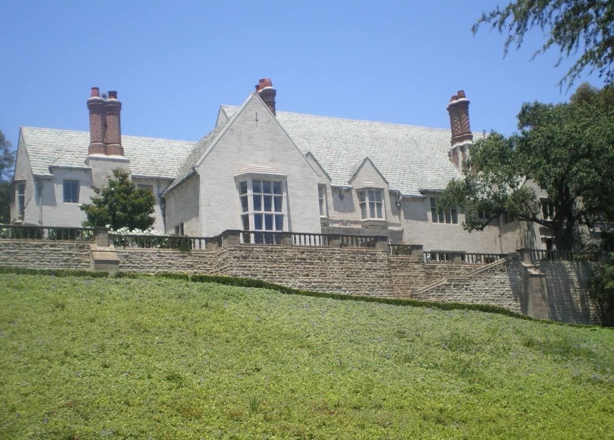 A grey stone Tudor-style mansion above a sloping lawn
