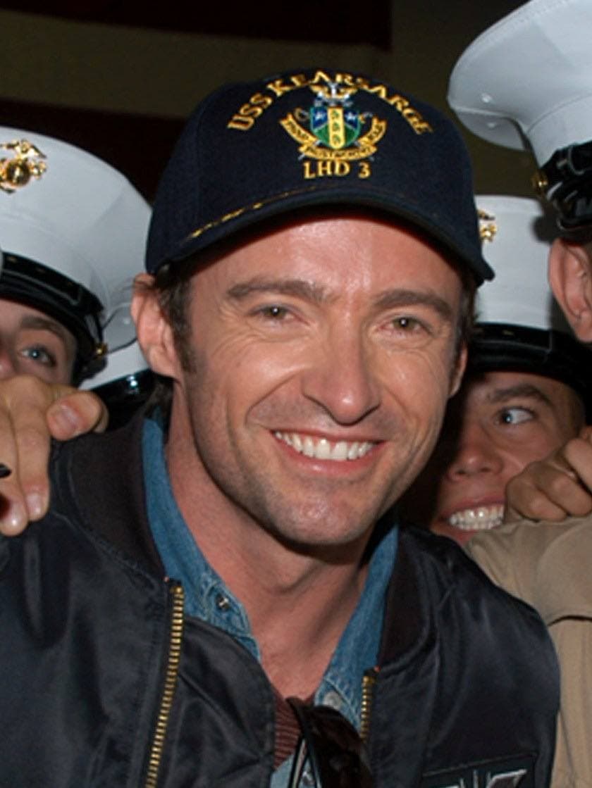 Hugh Jackman smiling in a navy cap, with sailors behind him