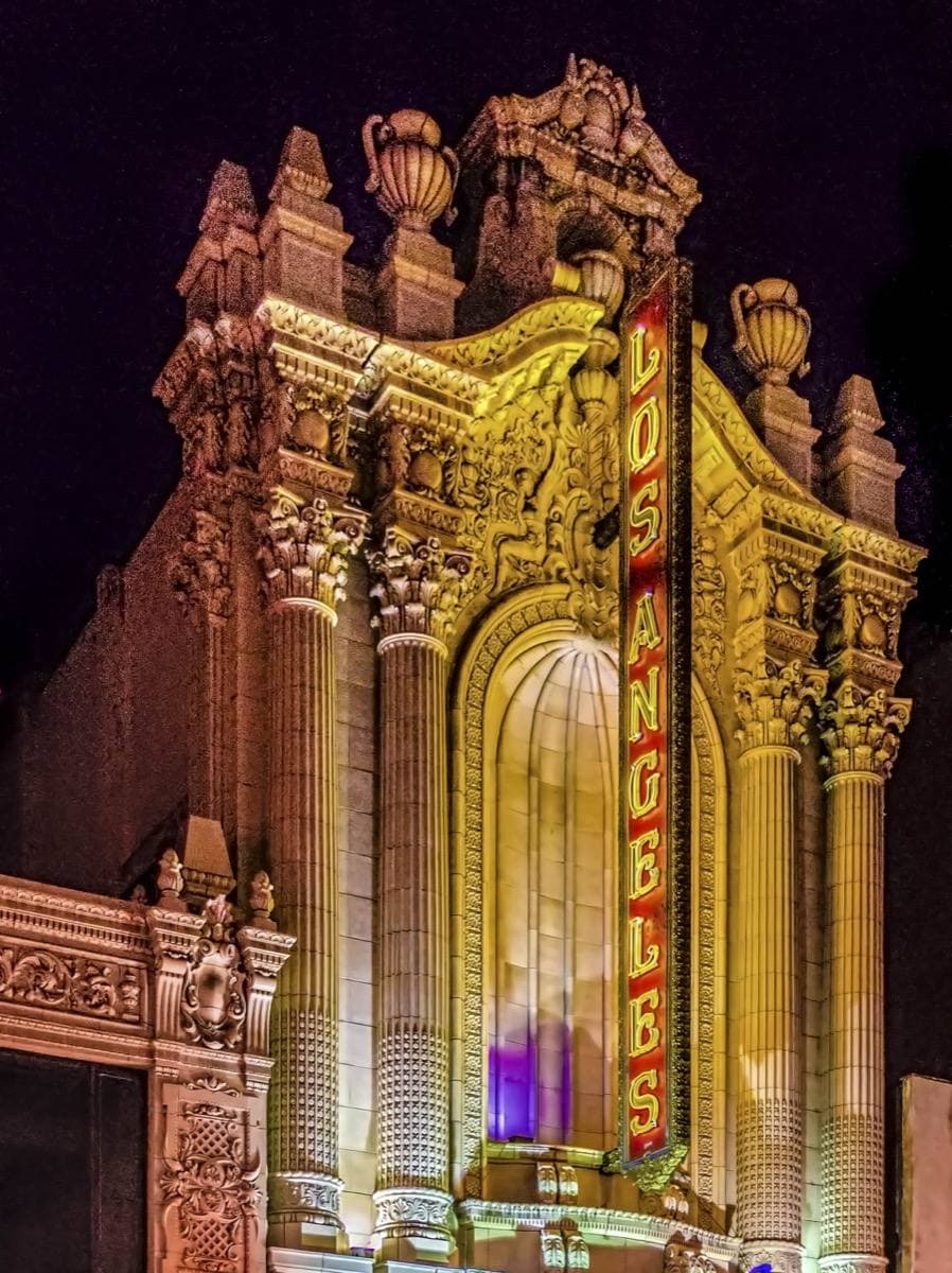A gilded theatre facade with a tall lit sign at night