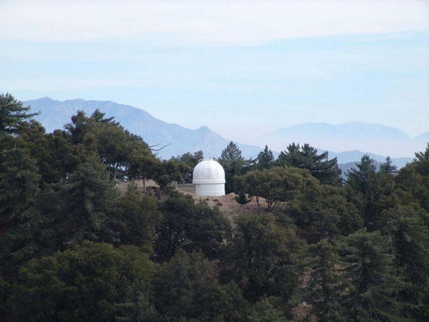 A white observatory dome among pine trees with mountains behind