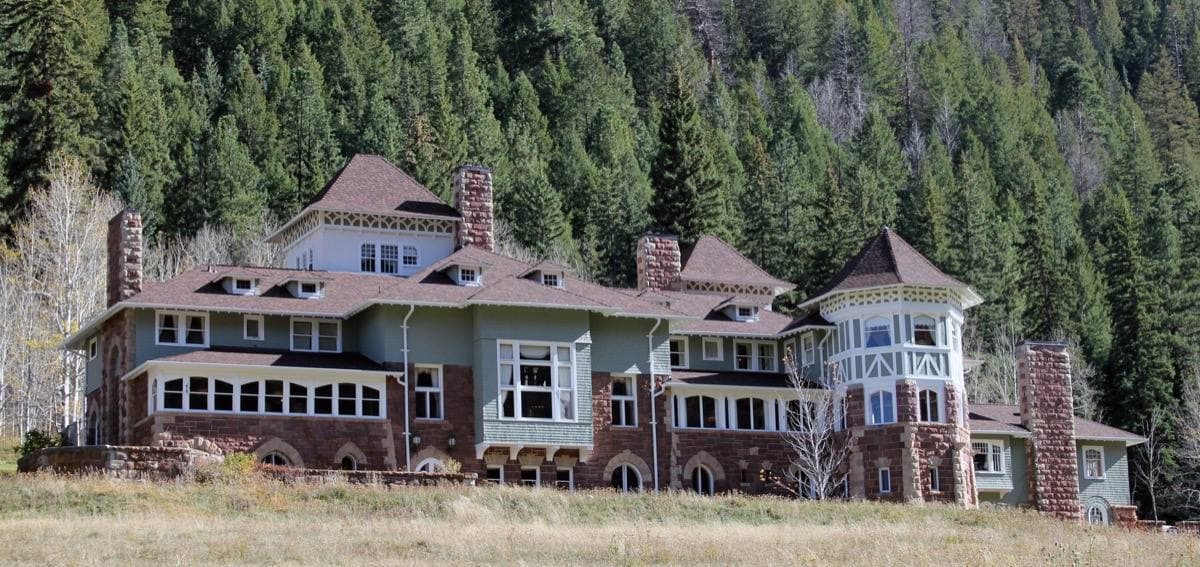 A long red-roofed mansion against a dark pine hillside