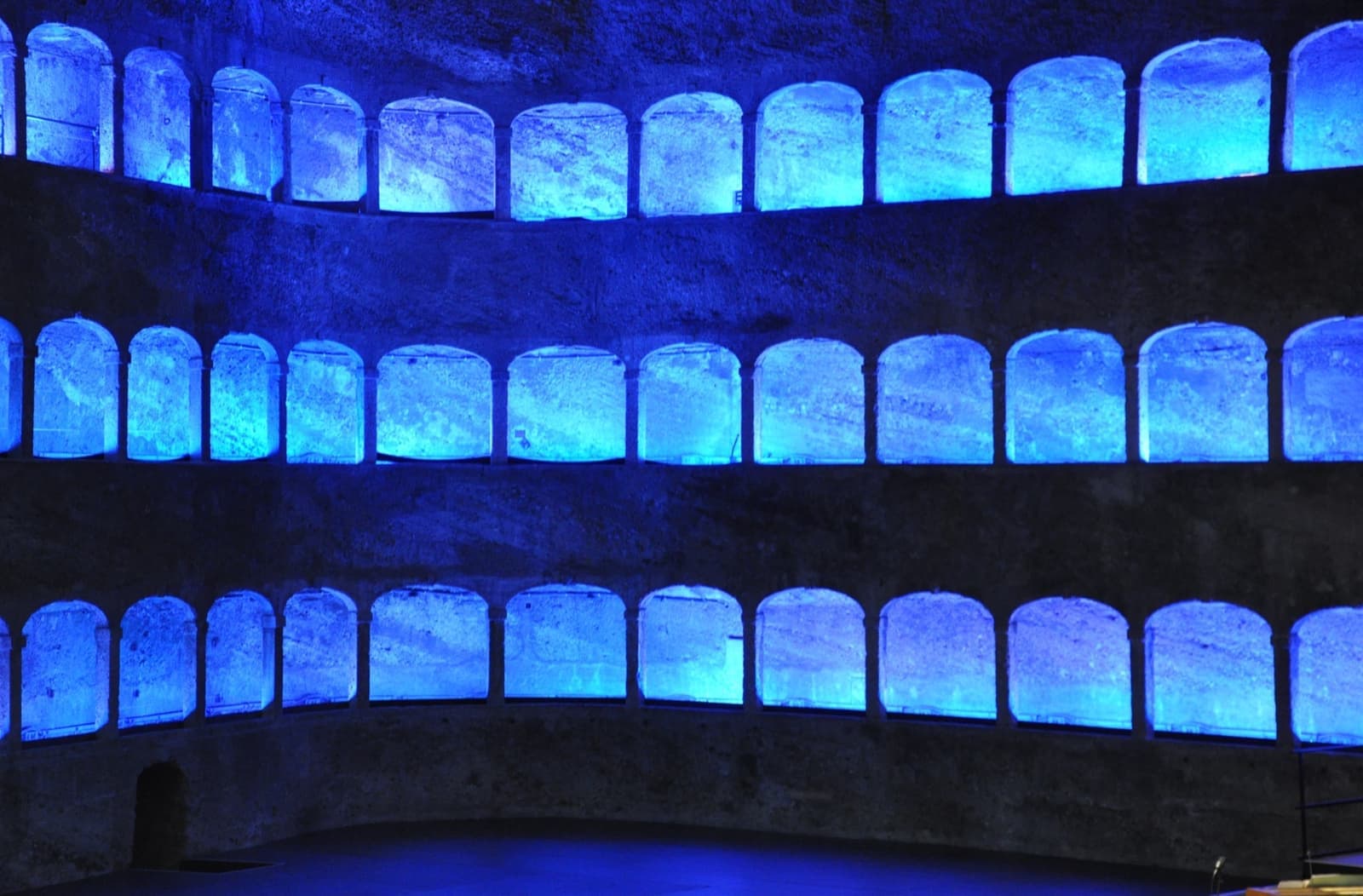 Three tiers of arches cut into a rock wall, lit blue