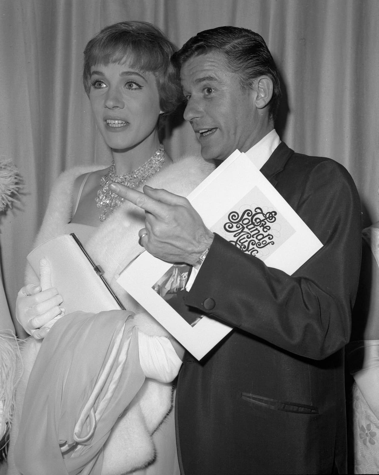 Julie Andrews in a fur wrap beside Roddy McDowall holding a programme