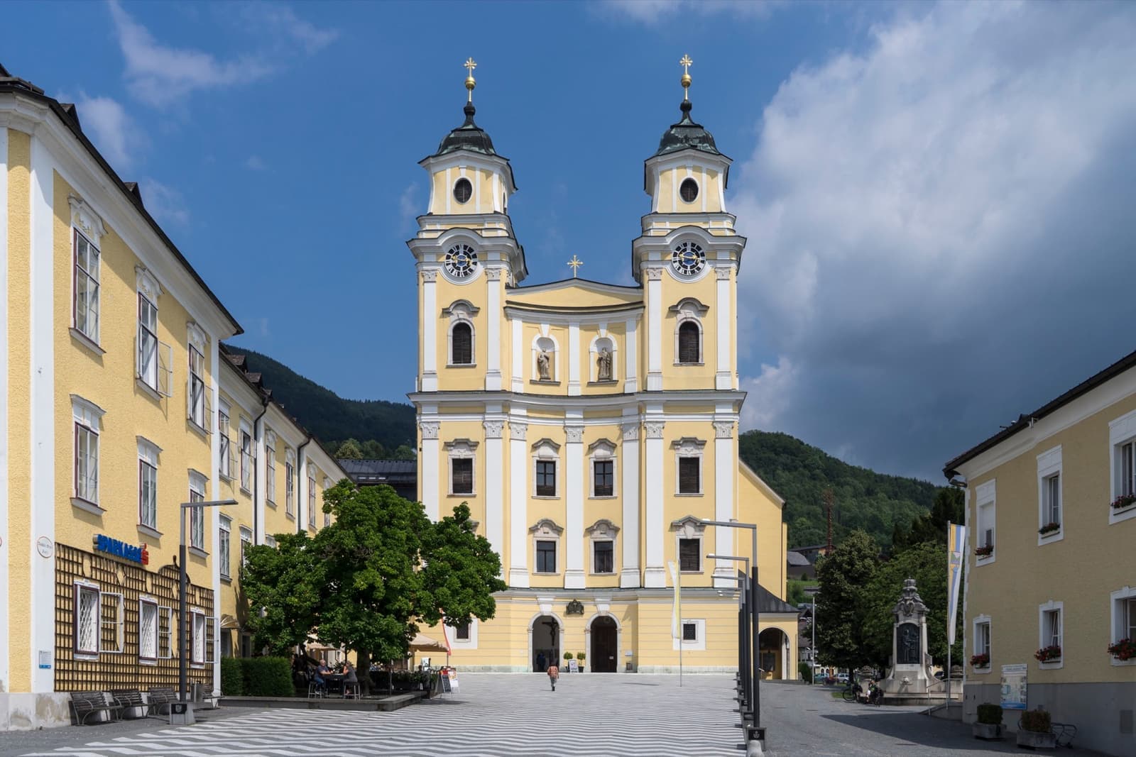 A yellow and white baroque church with two green-domed towers
