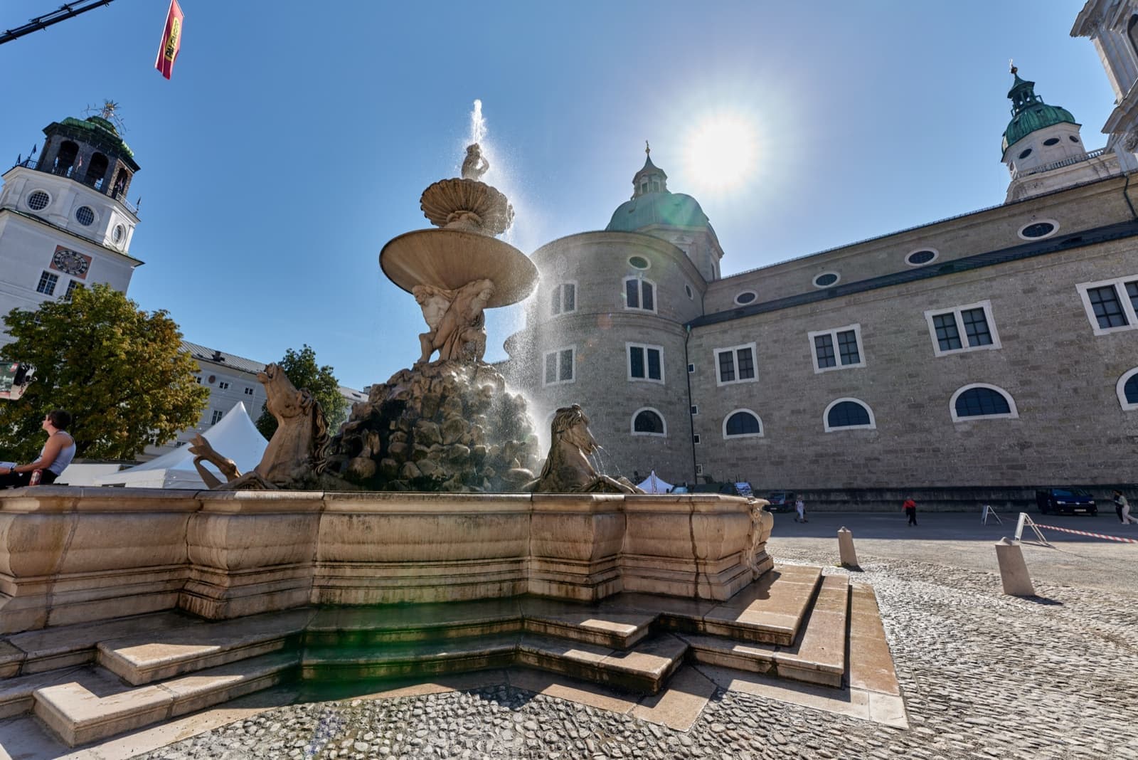 A tall baroque fountain with marble horses in a cobbled square