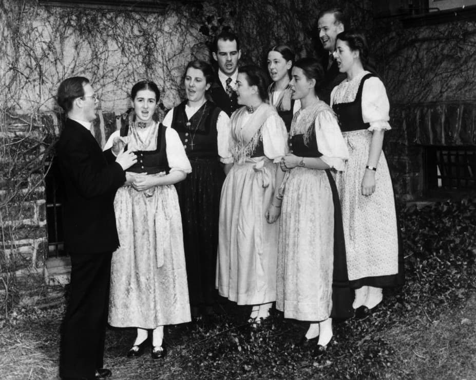 A family choir in dirndls and suits gathered around a conductor
