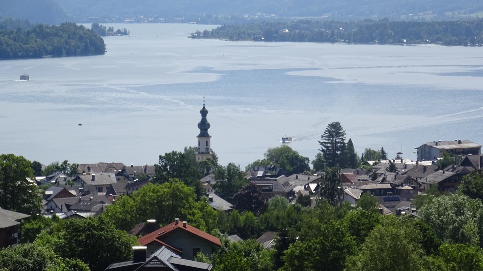 A church spire and village roofs above a wide lake