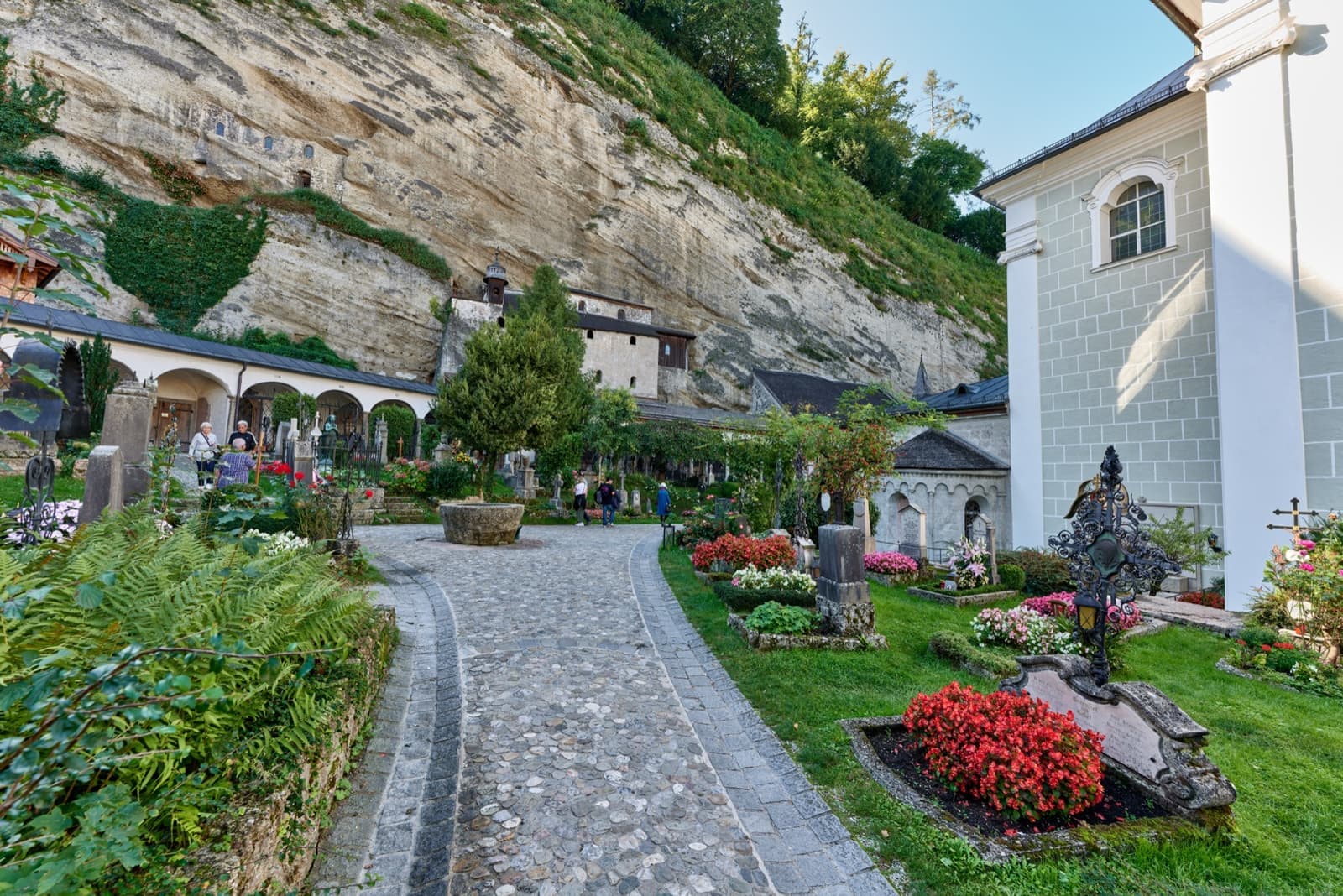 A cobbled path between flowered graves below a rock face