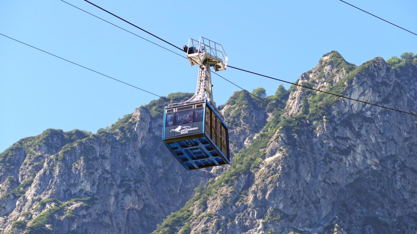 A cable car cabin hanging in front of grey limestone cliffs