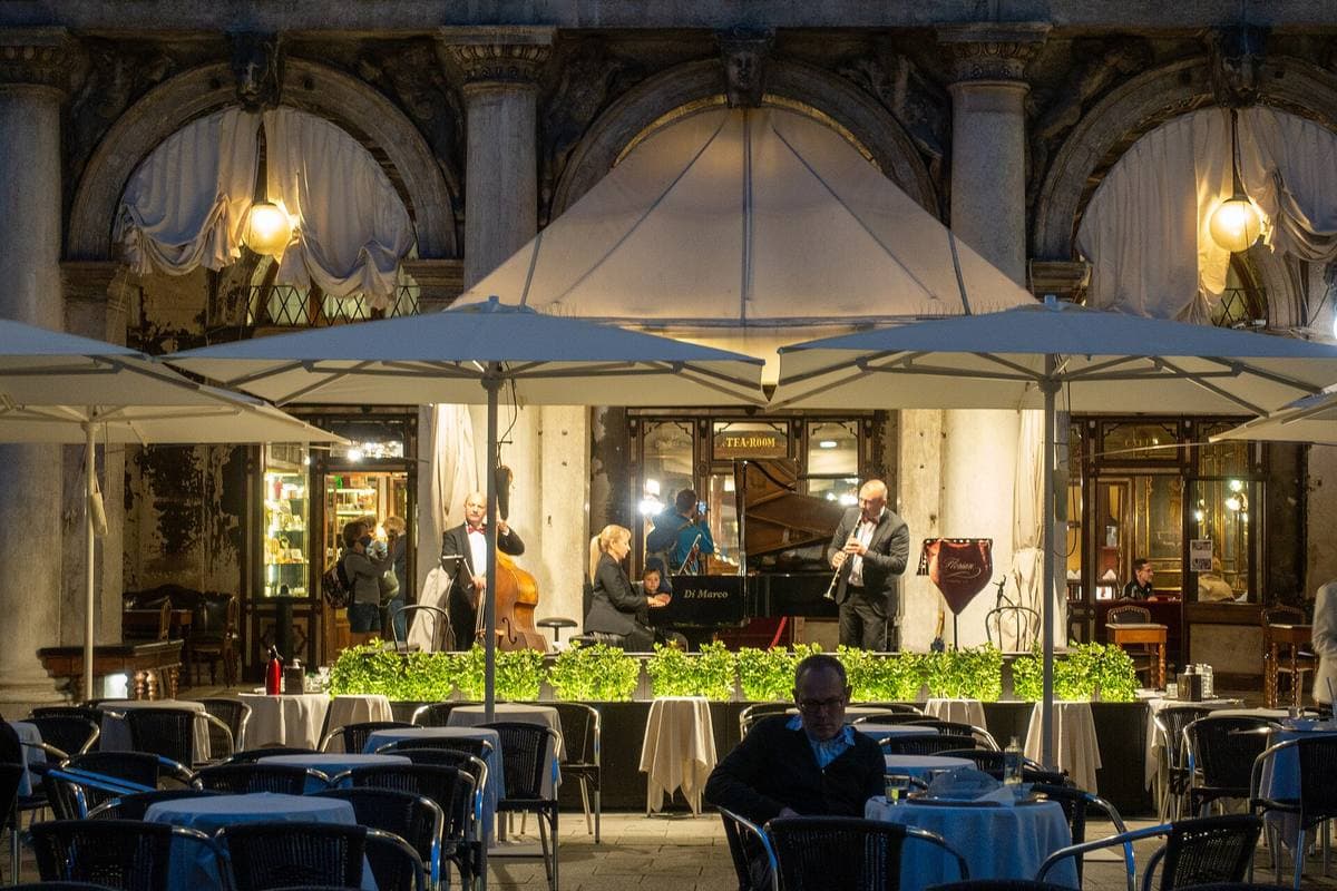 Café tables under the arcades of a long Venetian square