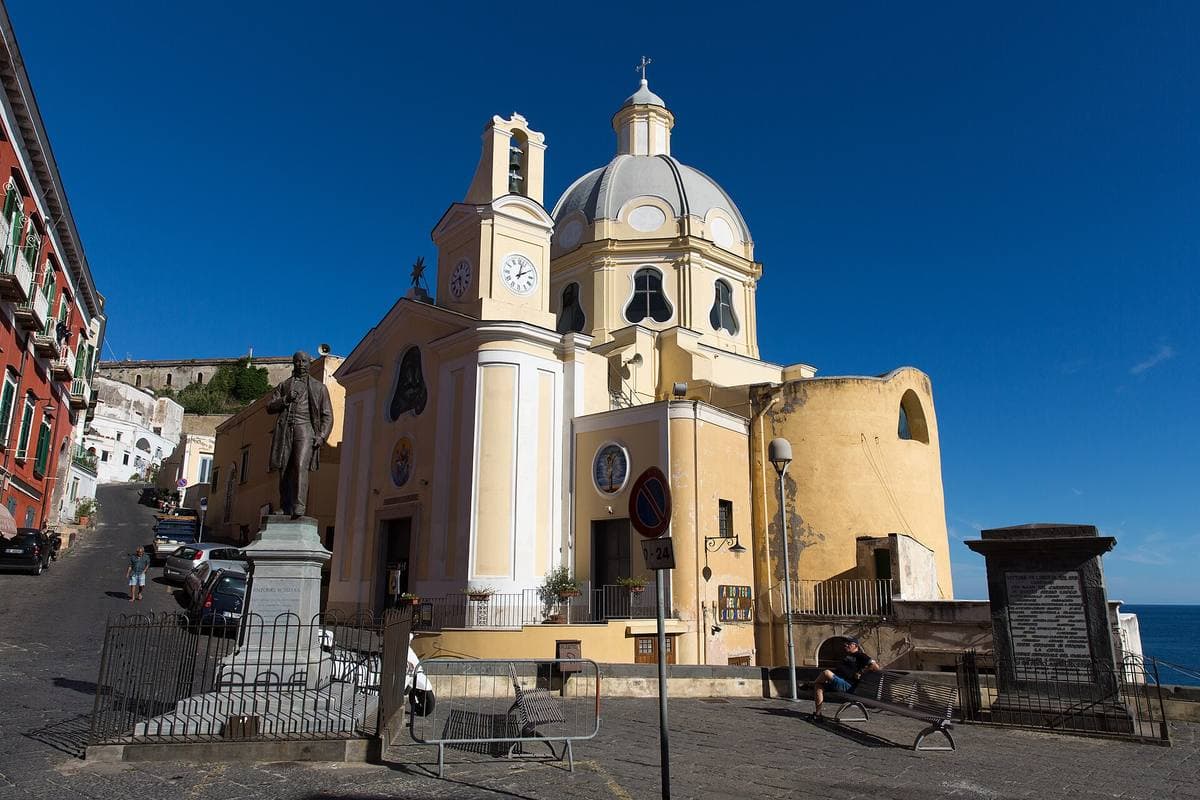 A domed church painted pale yellow on the cliff above the coloured houses of Corricella