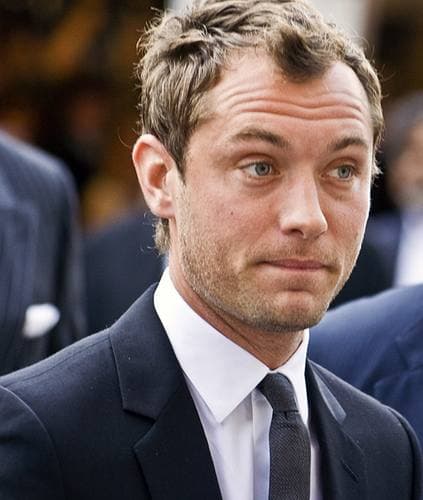 Jude Law in a dark suit and tie, looking just off camera