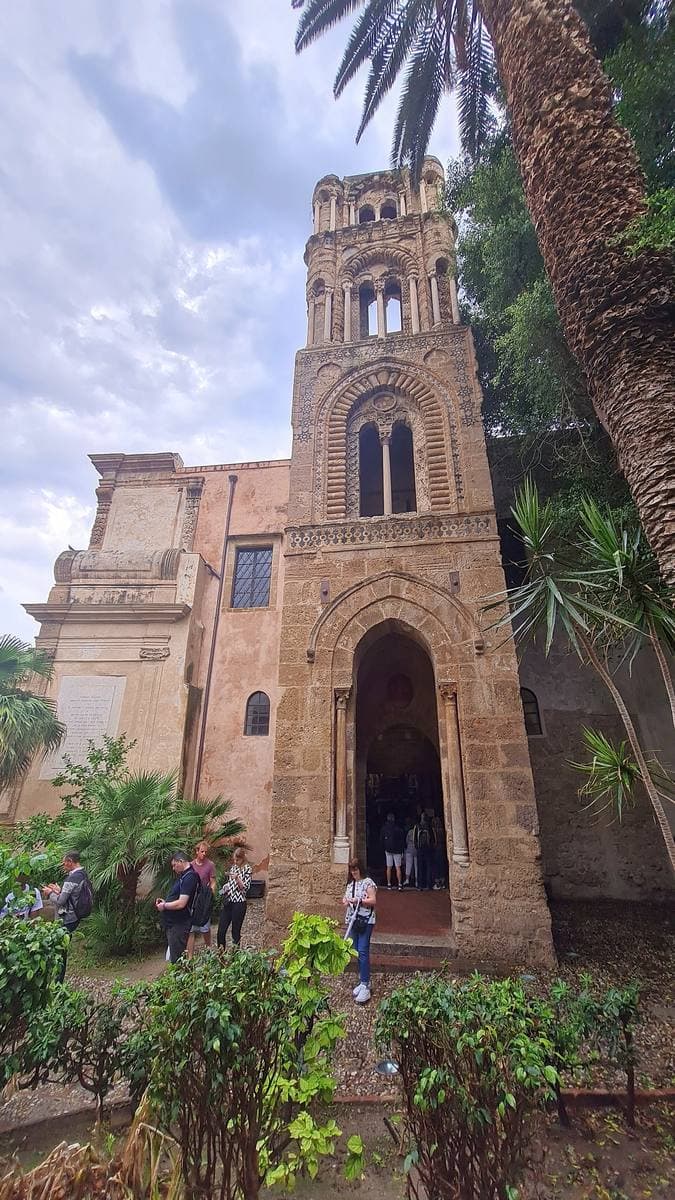 A Norman church with a stone bell tower above a small square in Palermo