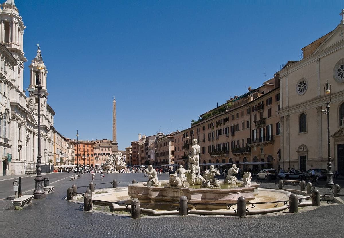 A long Roman square with a fountain and an obelisk in front of a domed church