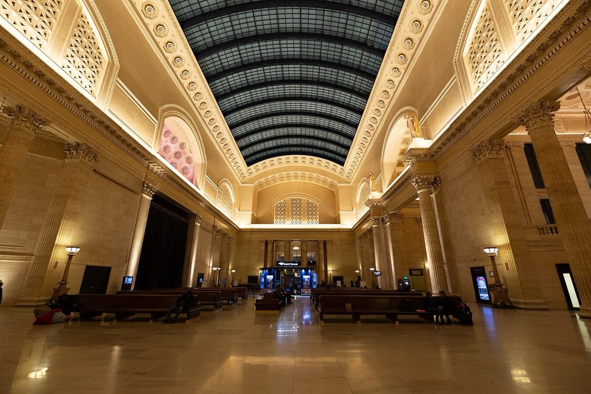 A tall station hall with a skylight, benches and stone columns