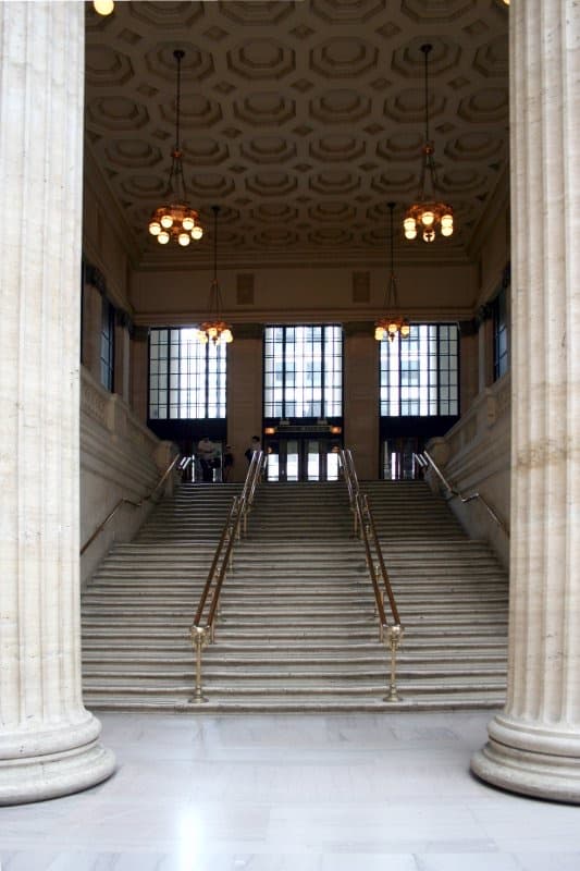 A wide marble staircase between stone columns in a station hall