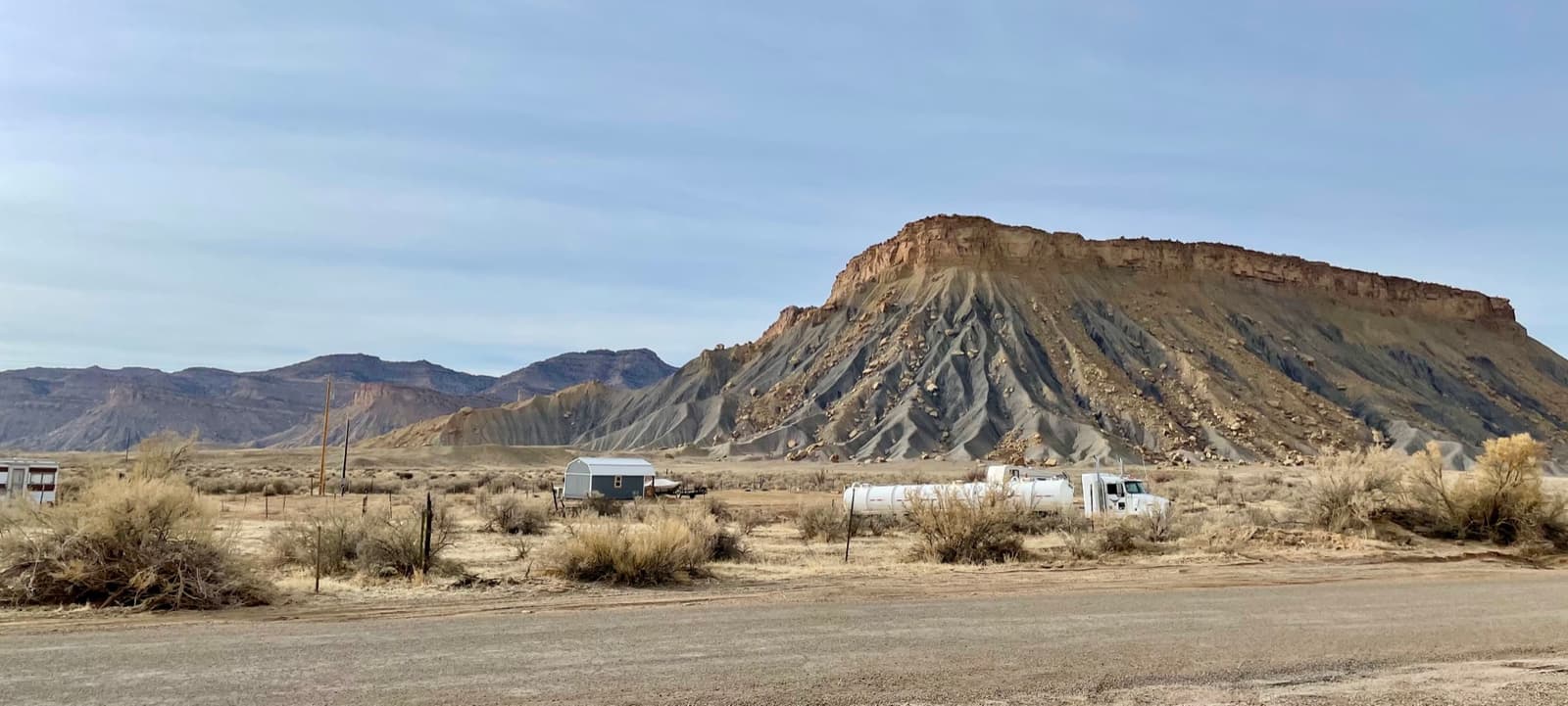 Grey banded cliffs rising behind scrub and a few low buildings