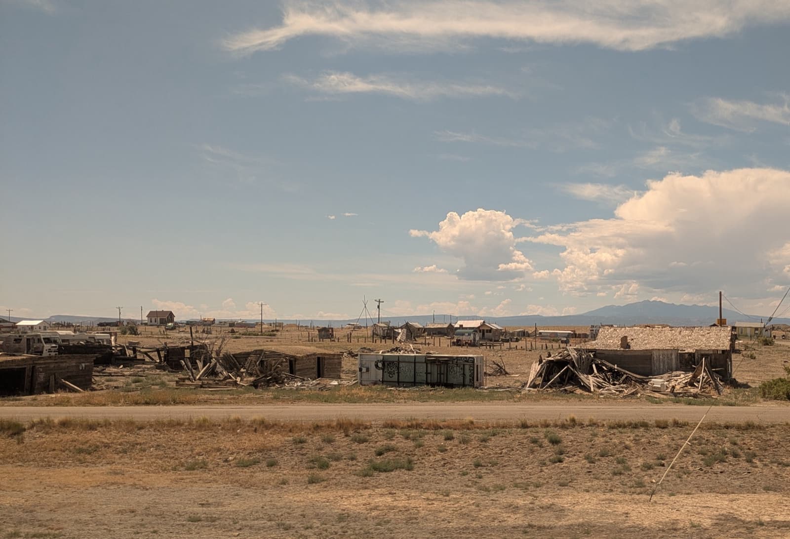 Weathered wooden shacks and wrecks strung along a flat desert horizon